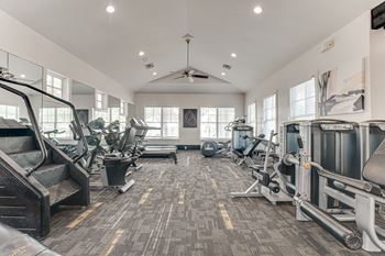 A spacious gym with a variety of equipment and a ceiling fan.